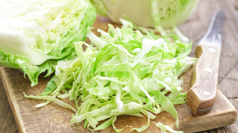 Shredded cabbage on a wooden cutting board next to a knife.
