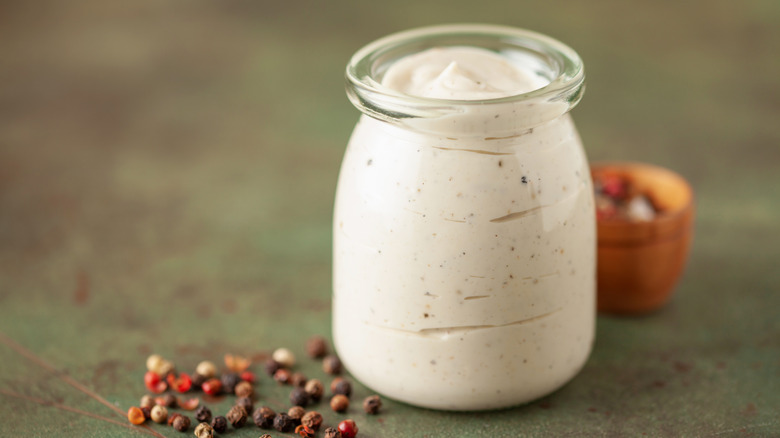 a jar of homemade Alabama white sauce next to peppercorns on a table