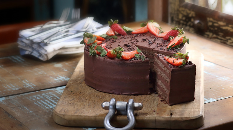 chocolate layer cake with strawberries and chocolate pieces on wood board