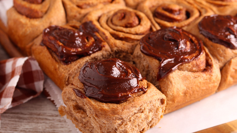 A pan of cinnamon rolls with several of them covered with chocolate frosting.
