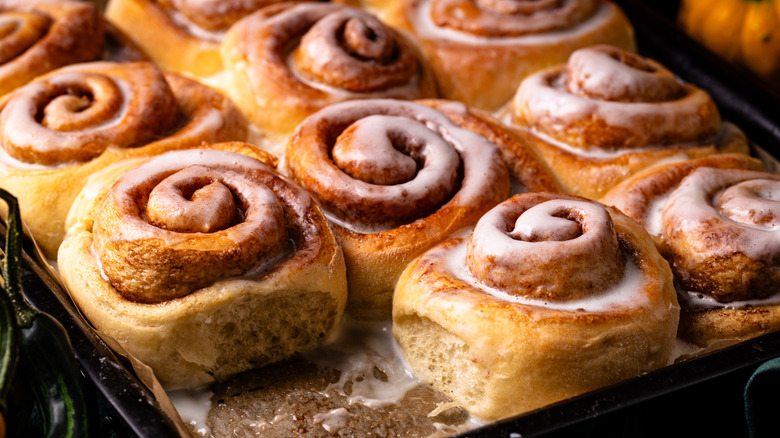 A tray of gooey, puffy cinnamon rolls topped with glaze with one removed