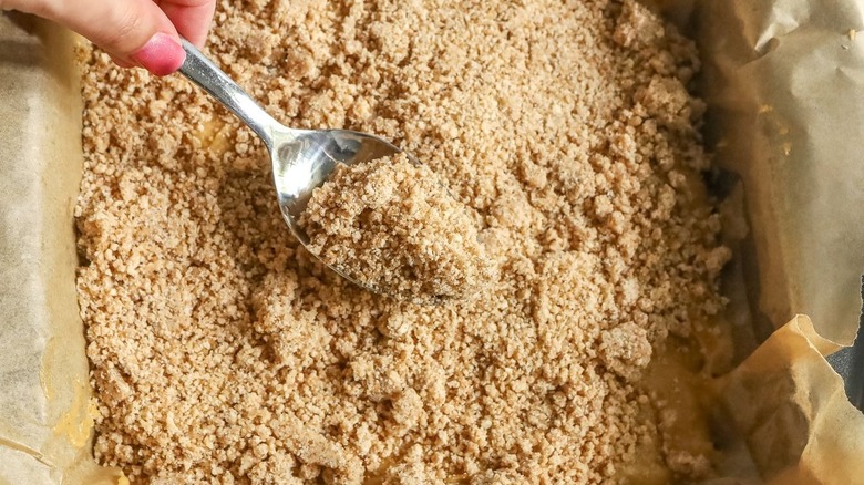 Hand spooning crumb topping onto coffee cake