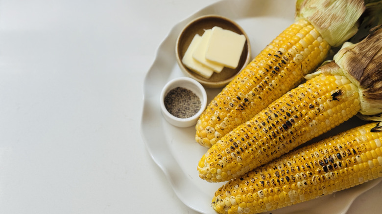 Grilled corn on the cob on a white platter with butter and pepper.