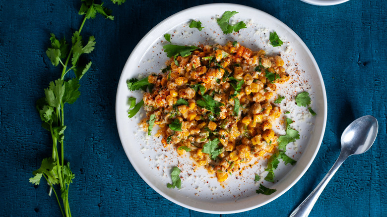 a plate of esquites topped with fresh cilantro against a dark blue background