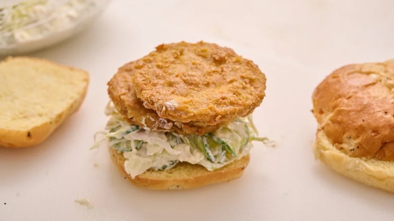 An open fried green tomato sandwich with coleslaw on a white surface next to another open sandwich