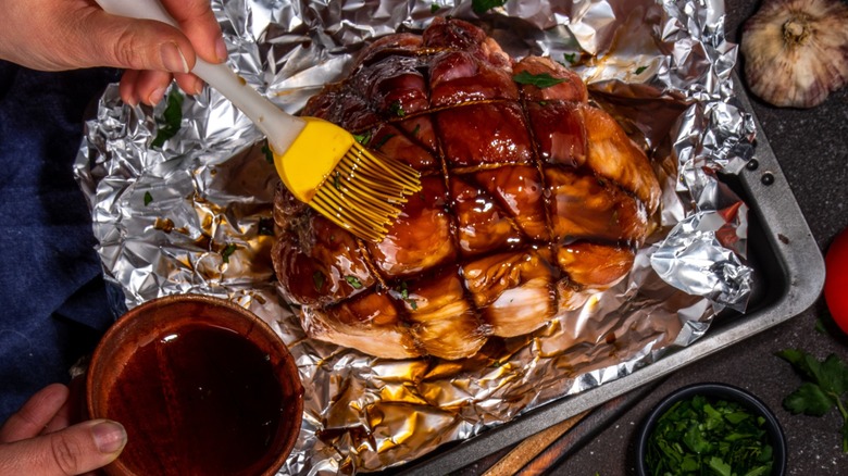 Glazing a ham with brush in one hand and a bowl of sauce in the other
