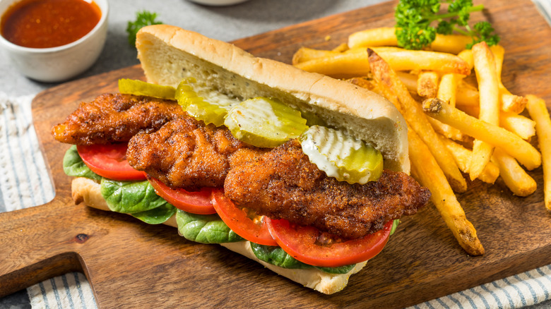A fish sandwich with tomatoes and pickles, and some fries on the side