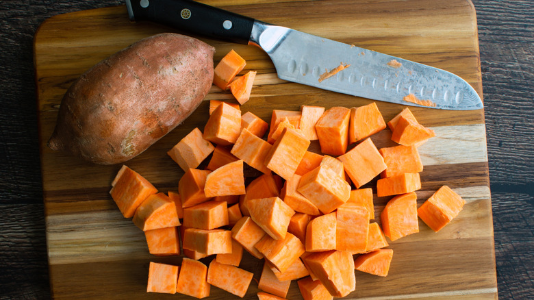 Chopped sweet potato on wooden cutting board next to whole spud and knife