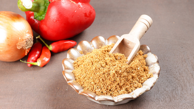 Cajun seasoning in a bowl with wooden spoon, next to peppers and onions