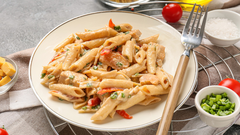 A plate of creamy Cajun-spiced chicken pasta next to bowls filled with ingredients