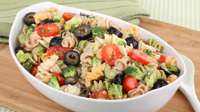 A white oblong bowl filled with colorful, fresh pasta salad made from rotini and vegetables