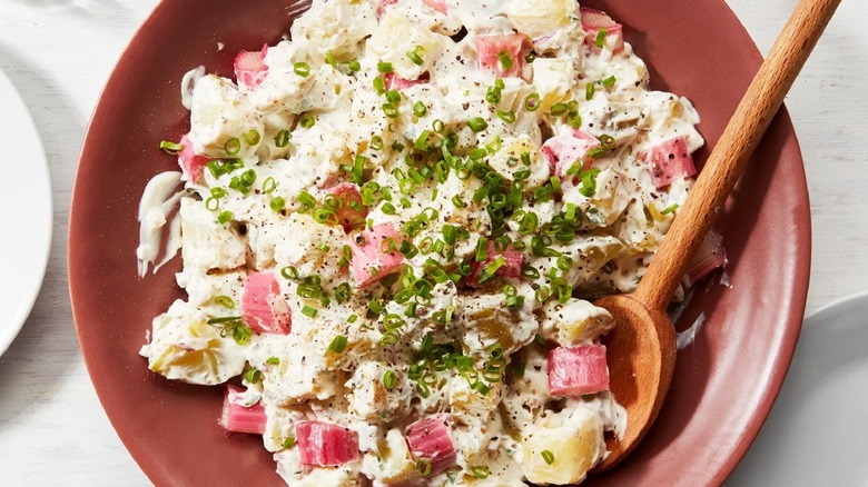 A bowl of rhubarb potato salad with a wooden spoon
