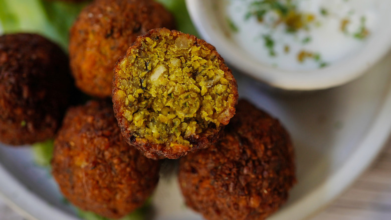 falafel balls, one sliced in half, on a plate with a yogurt sauce in the background