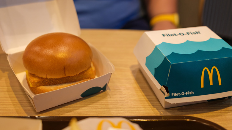 Open Filet-O-Fish box with a sandwich inside on a wooden table beside a closed Filet-O-Fish box