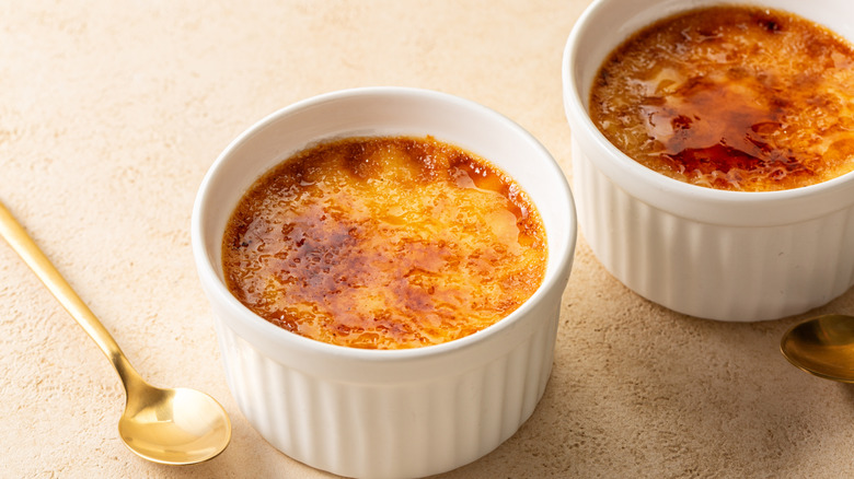 Two white ramekins filled with creme brulee next to golden spoon