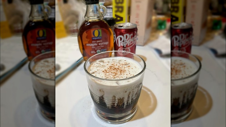 Creamy drink in glass with maple syrup bottle, Dr Pepper can