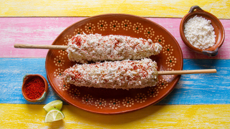 two cobs of elote topped with plenty of cheese and ground chile