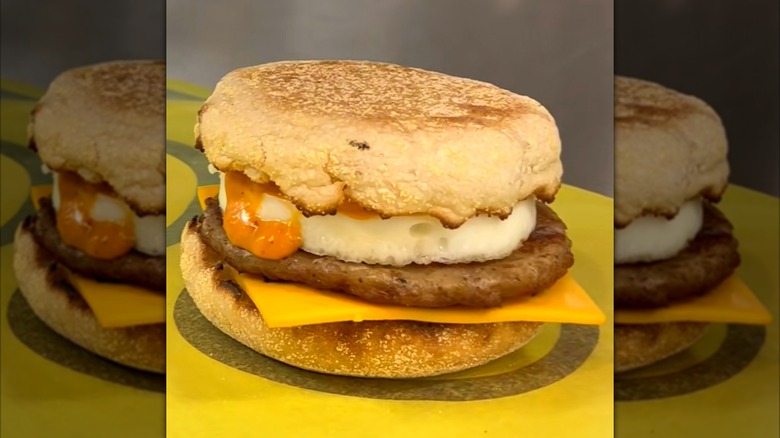 McDonald's Egg McMuffin sandwich with egg, cheese, sausage,  and orange chili sauce sitting on yellow surface