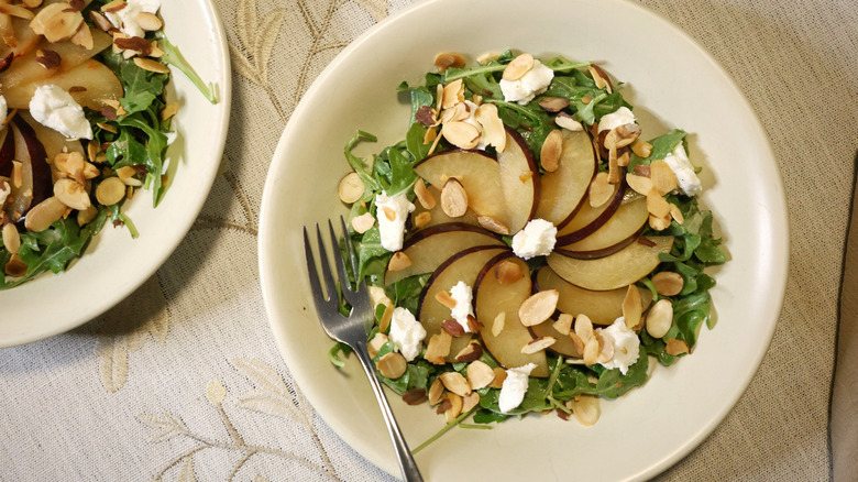 an overhead view of two arugula salads with plums, chèvre, and sliced almonds