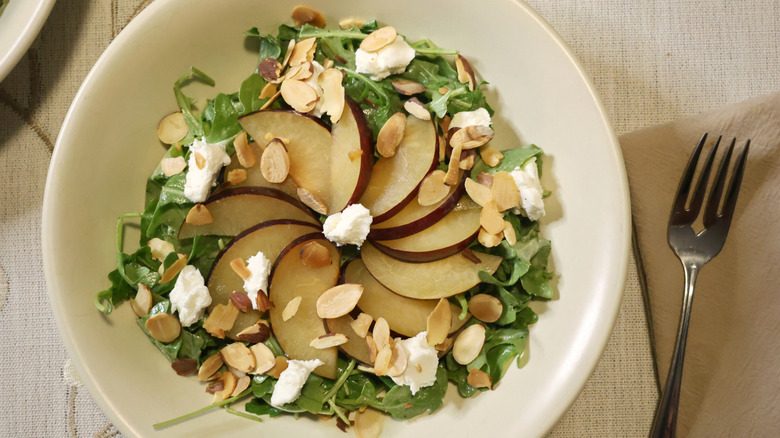 and overhead view of a salad of dressed arugula, sliced plums, sliced almonds, and chèvre