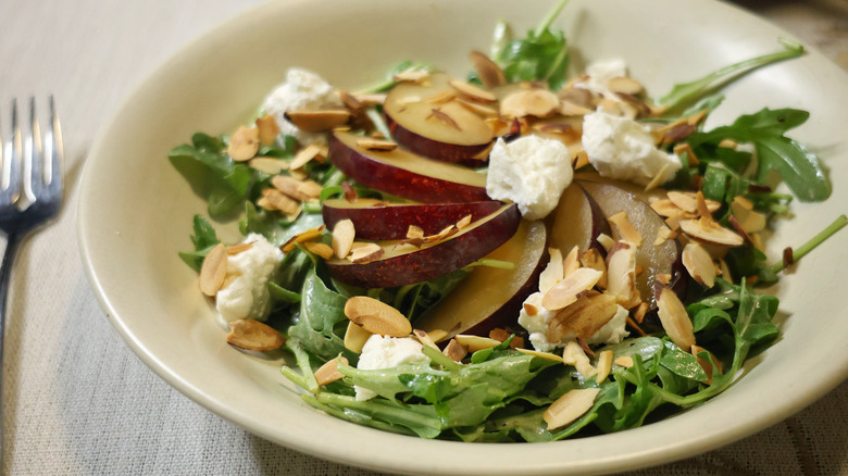 a close-up of an arugula salad with sliced almonds, plums, and chèvre