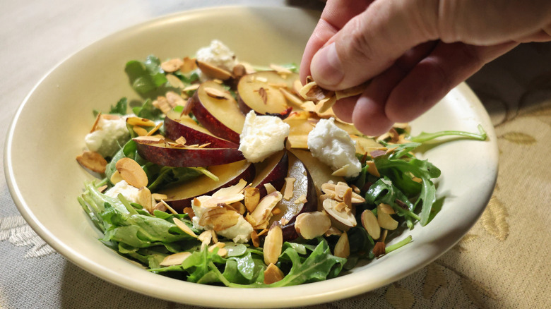 a hand sprinkling toasted sliced almonds onto a salad