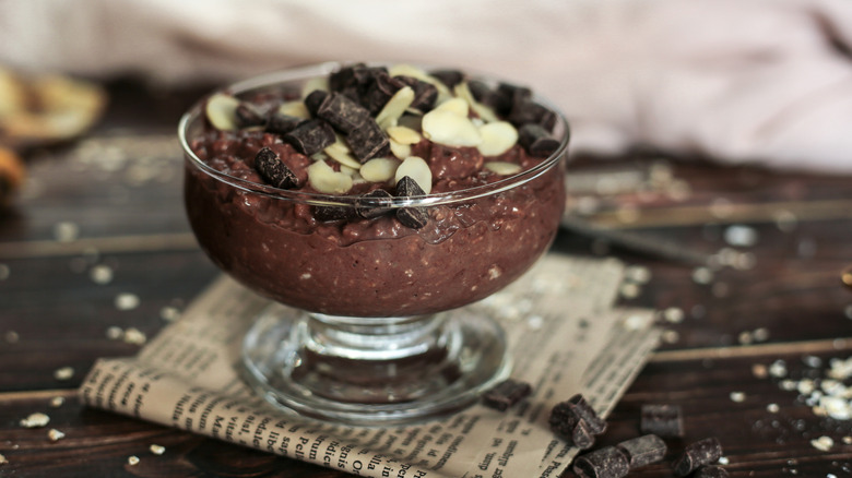 a glass dish of chocolate oatmeal topped with sliced almonds and chocolate chunks