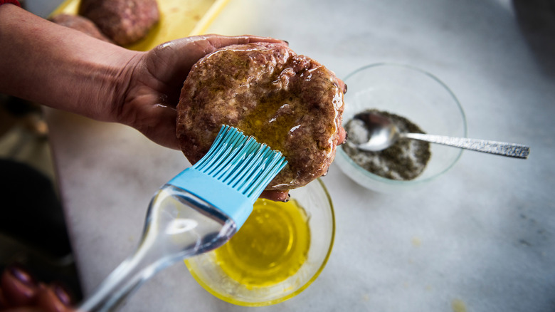 Foodie brushing a burger patty with olive oil