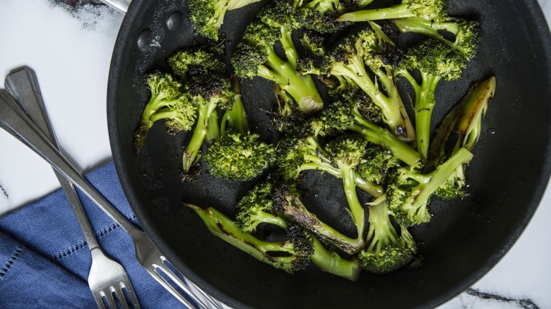 Charred broccoli in skillet next to forks