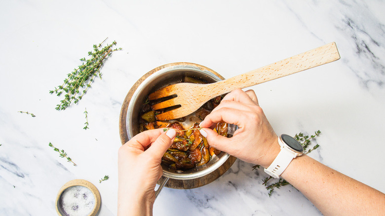 Adding fresh thyme to saucepan with compote.