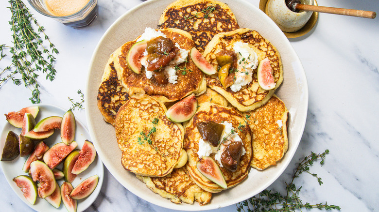 A plate full of goat cheese pancakes on the table with fresh figs, honey and coffee.