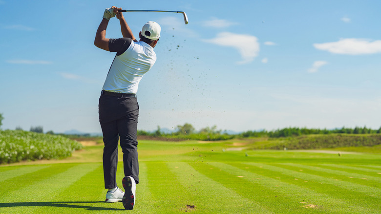 Person hitting a golf ball into a field