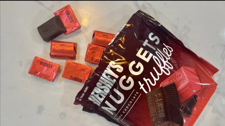 An opened bag of Hershey's Nuggets Dark Chocolate Truffles with a few spilled onto the counter beside it