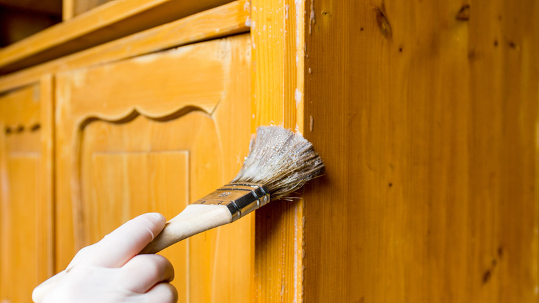 A person in gloves applying a coat of sealant to wooden cabinets