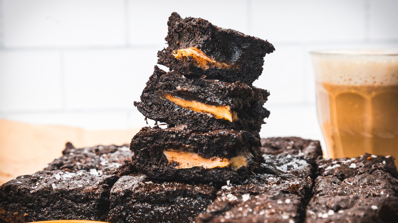 Tower of gooey caramel-filled brownies with coffee in background.