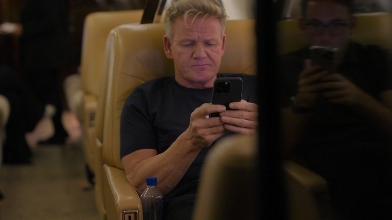 Chef Gordon Ramsay looking at a cell phone while sitting on a plane