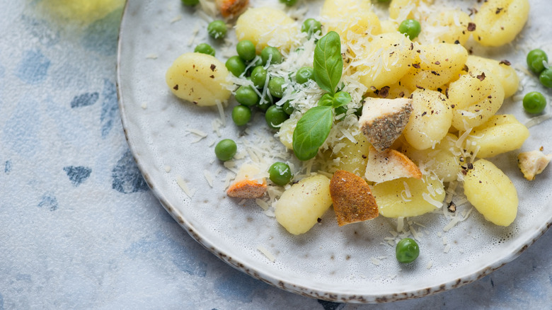 Close-up of gnocchi with peas and Parmesan and croutons on white stone plate.