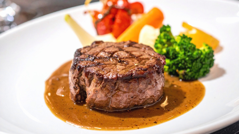 Seared filet mignon in brown sauce on white plate.