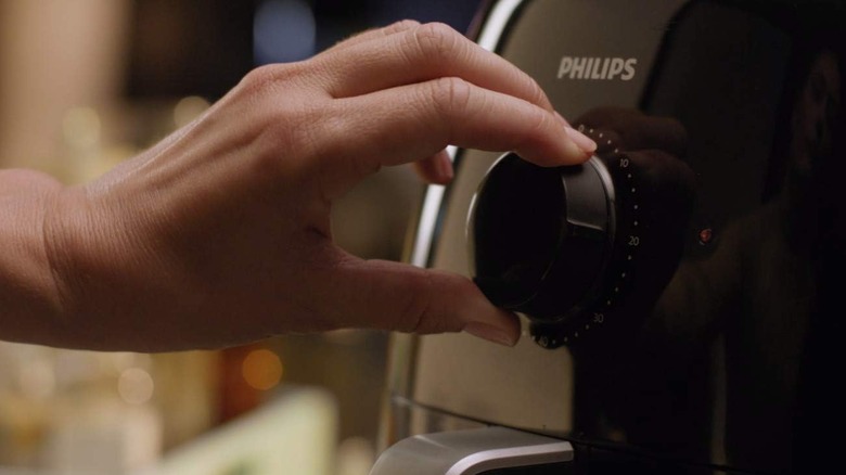 closeup of a woman's hand turning the timer dial on a Phillips XXL air fryer