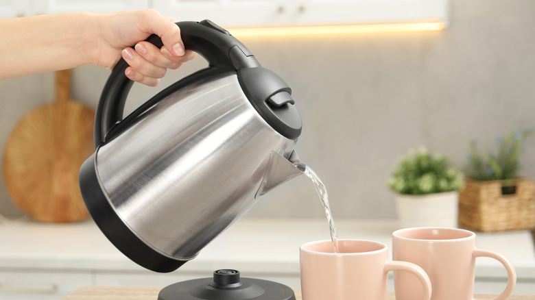 woman's hand pouring hot water from an electric kettle into a pair of pink mugs