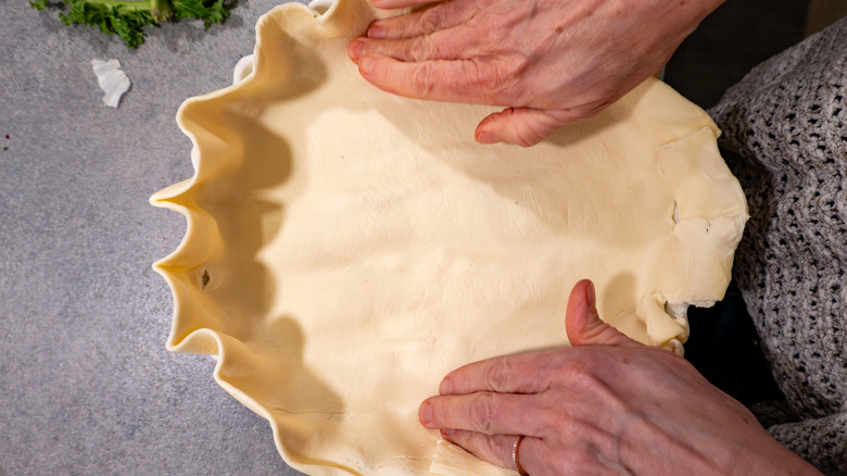 Person fitting a quiche crust into a pan
