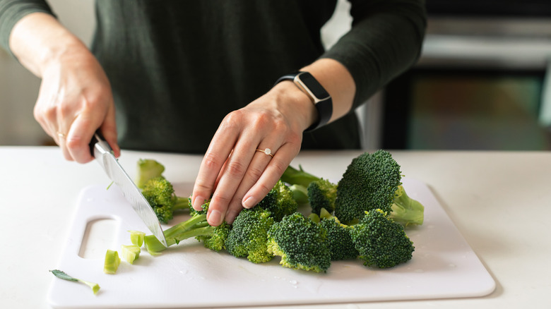 hands chopping broccoli stems on white chopping board