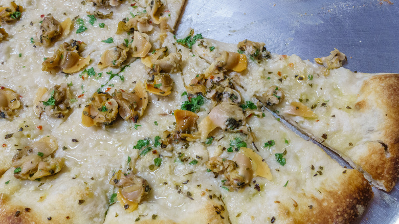 A partially sliced pizza with clams, or white clam pie