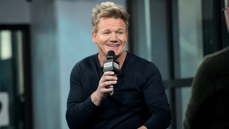 Chef and TV host Gordon Ramsay holds a microphone and smiles as he is interviewed