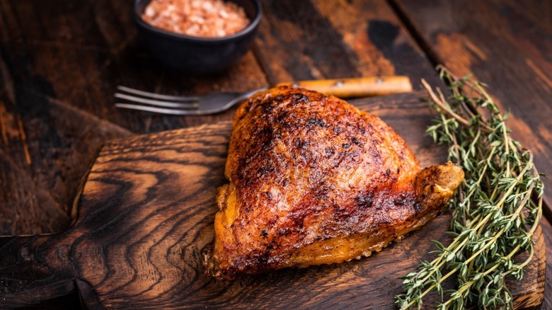 a cooked chicken thigh on a board wwith some rosemary