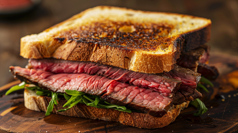 a sliced steak sandwich with arugula on toasted bread