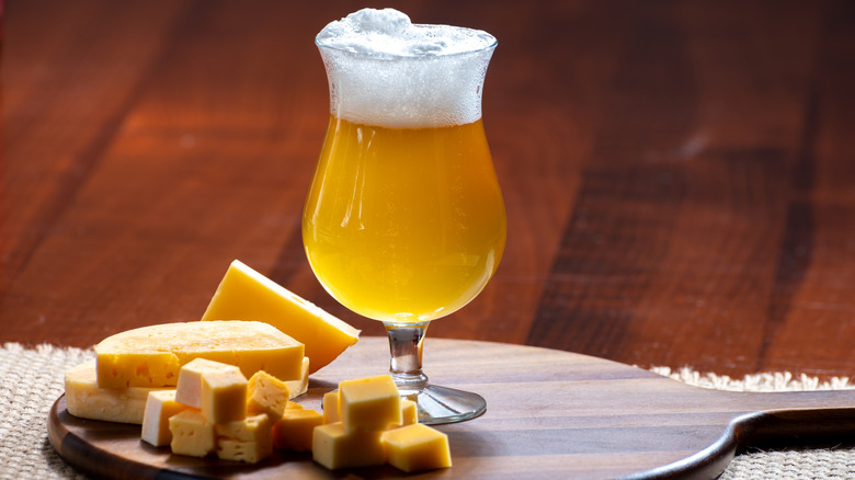 a light foamy beer on a cutting board with various cheeses