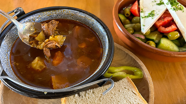 Traditional Hungarian goulash served in a black pot with a garnish of pepper and slice of bread
