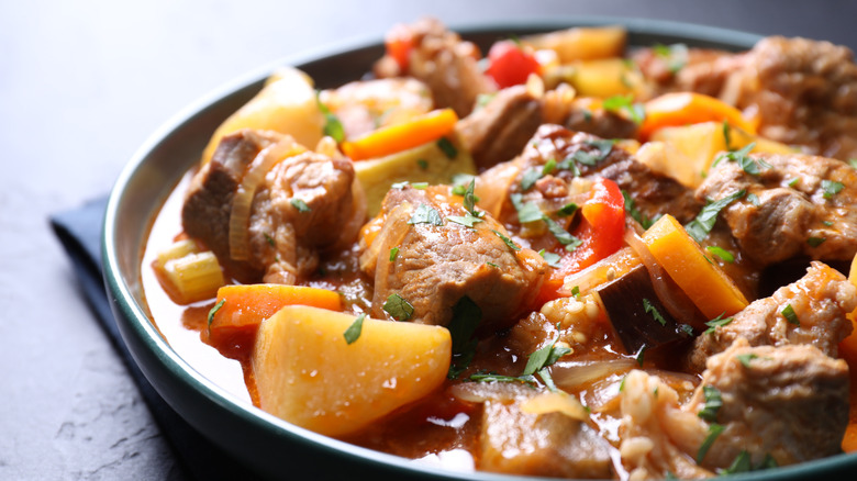 A large, shallow bowl holding an overfilling serving of beef stew with potatoes, carrots, and celery