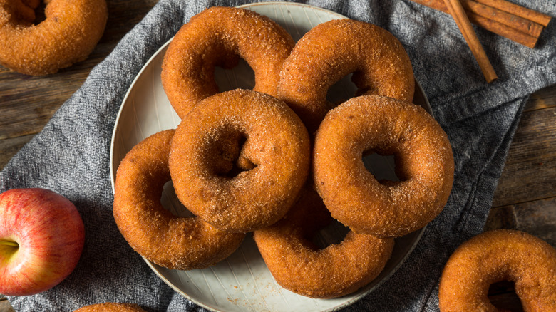 A plate piled high with apple cider donuts surrounded by apples